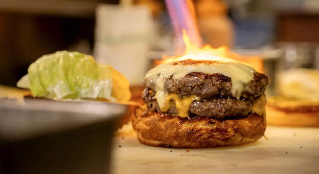 チーズがとろけるジューシーなパティを炙る調理シーン